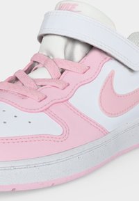 Primo piano di una sneaker Nike rosa e bianca con lacci e una fascia in velcro bianca su sfondo bianco.