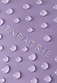 Materiaal in paars met een gestructureerd oppervlak en verhoogde druppels, waarop het woord "EXPATRIÉ" in metallic groen is geperst. Gladde en glanzende afwerking op de druppels.