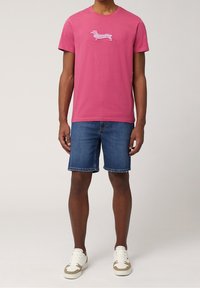 Rosa Baumwoll-T-Shirt mit gestreiftem Dackel-Design, kombiniert mit Denim-Shorts und weißen Sneakern, präsentiert einen lässigen Sommerlook.