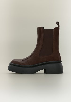 Dark brown suede ankle boot with black elastic side panels, thick black platform sole, and pull tab at the back.