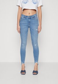 Light blue skinny jeans with a distressed hem, featuring a high waist and slight fading, paired with navy embellished open-toe heels.