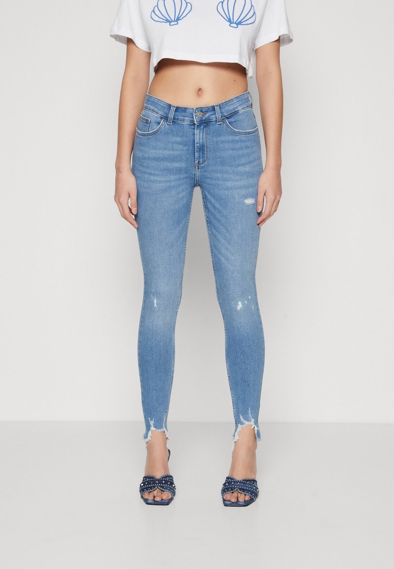 Light blue skinny jeans with a distressed hem, featuring a high waist and slight fading, paired with navy embellished open-toe heels.