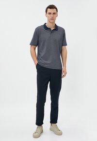 Polo de color azul marino con un patrón texturizado, de manga corta y con cuello; combinado con pantalones oscuros y zapatillas de color claro.