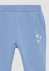 Hellblaue Jogginghose mit weichem Material, ausgestattet mit einem kleinen gestickten Design aus drei weißen Herzen am linken Oberschenkel und seitlichen Taschen.