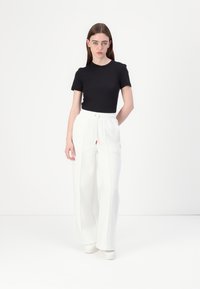 Camiseta negra de manga corta combinada con pantalones anchos blancos, con una cinturilla elástica y detalles en rojo, sobre un fondo liso.