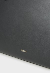 Mustapohjainen nahkalaukku, jossa on sileä pinta ja kultainen "Furla"-logo. Suunnittelu on minimalismia, ja siinä on siistit viivat.
