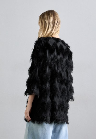 Melna mākslīgā kažokā ar teksturētu, zigzag rakstu, vaļīgām piedurknēm un brīvu piegriezumu. Valkāta pār gaiši zilu, platu kāju džinsu biksēm.