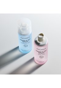 Due bottiglie spray etichettate "GOSH PRIME'N SET SPRAY" per una pelle rinfrescata e luminosa, una blu e una rosa, che proiettano ombre su una superficie bianca.