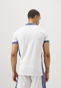 Polo blanco de mangas cortas con un patrón texturizado, detalles en color marino en el cuello y las mangas, y un sutil logo en el dobladillo.