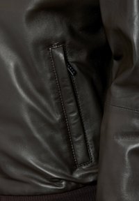 Donkerbruine leren jas met een zijvak, een gladde afwerking, subtiele stiksels en een geribde zoom voor extra textuur.