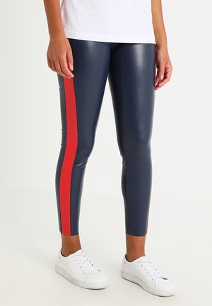 Navy faux leather leggings with a red side stripe, fitted design, smooth texture, and paired with white sneakers.
