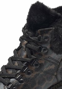 Bottine cheville à imprimé léopard noir et marron avec une finition brillante, un col en fourrure et des lacets noirs fixés par des œillets en métal. Semelle épaisse.