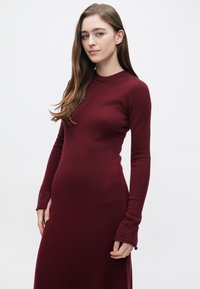 Bordowa sukienka swetrowa z długim rękawem, dopasowaną górą i rozkloszowanym dołem. Dzianinowa tkanina o fakturze z delikatnym prążkowaniem przy dekolcie i mankietach.