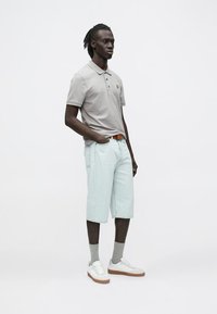 Sivá polokošeľa s malým logom, svetlomodré krátke nohavice dĺžky po kolená, biele tenisky a sivé ponožky. Úzky strih a neformálny dizajn.