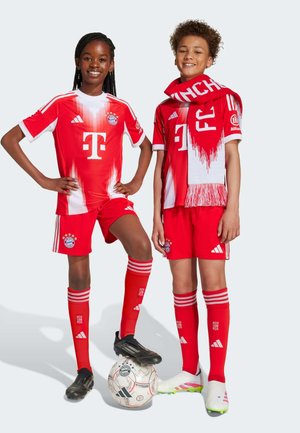 Rode voetbalshirts met witte accenten, short en sokken, met het logo van Bayern München. Spelers staan naast een voetbal.