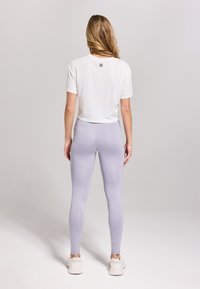 Witte korte mouwen cropped top met een logo op de rug, gecombineerd met lichtlila leggings, gladde textuur en een getailleerd design. Witte sneakers.