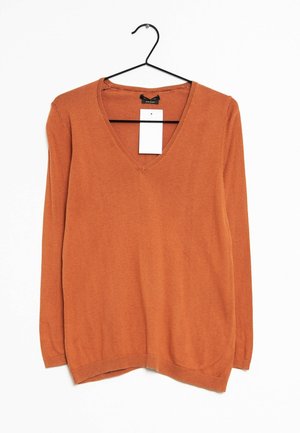 Pull à manches longues col en V couleur rouille suspendu sur un cintre noir avec une étiquette de prix rectangulaire blanche attachée au col.