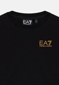 Schwarzes Baumwoll-T-Shirt mit Rundhalsausschnitt, das ein goldenes EA7 Emporio Armani-Logo auf der linken Brust zeigt. Glatte Textur, lässiges Design.