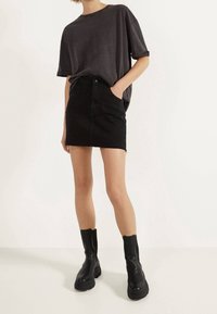 Zwarte cropped t-shirt met opgerolde mouwen, zwarte denim minirok met rafels aan de onderkant, en enkelhoge zwarte platformlaarzen.