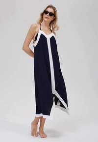 Marineblaues Kleid mit kontrastierender weißer Einfassung, lockerer Passform, Spaghettiträgern und asymmetrischem Saum. Glatter Stoff.