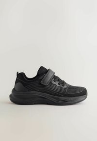 Baskets de sport noires en tissu texturé, lacets sur le devant et sangle Velcro réglable sur une semelle épaisse, vues de profil.