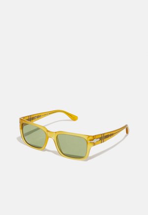 Occhiali da sole in plastica gialla con montatura quadrata, lenti verdi e dettagli a motivo sulle aste. Design leggero, superficie liscia.