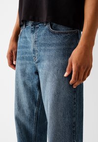 Ljust blå denimjeans med rak bendesign, fem fickor och subtila urtvättningar; har klassisk sömnad och en teksturerad tyglook.
