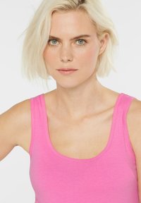 Enganliegendes pinkes Tanktop mit Rundhalsausschnitt, Schulterträgern und einer glatten, leichten Stofftextur.