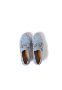 Scarpe slip-on azzurro chiaro con una texture liscia, punta arrotondata e una fibbia decorativa argentata sul fronte.
