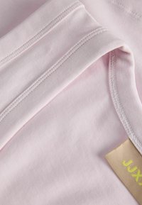 Tissu en coton rose clair avec bords pliés et coutures visibles, présentant une étiquette de vêtement beige et jaune partiellement visible.