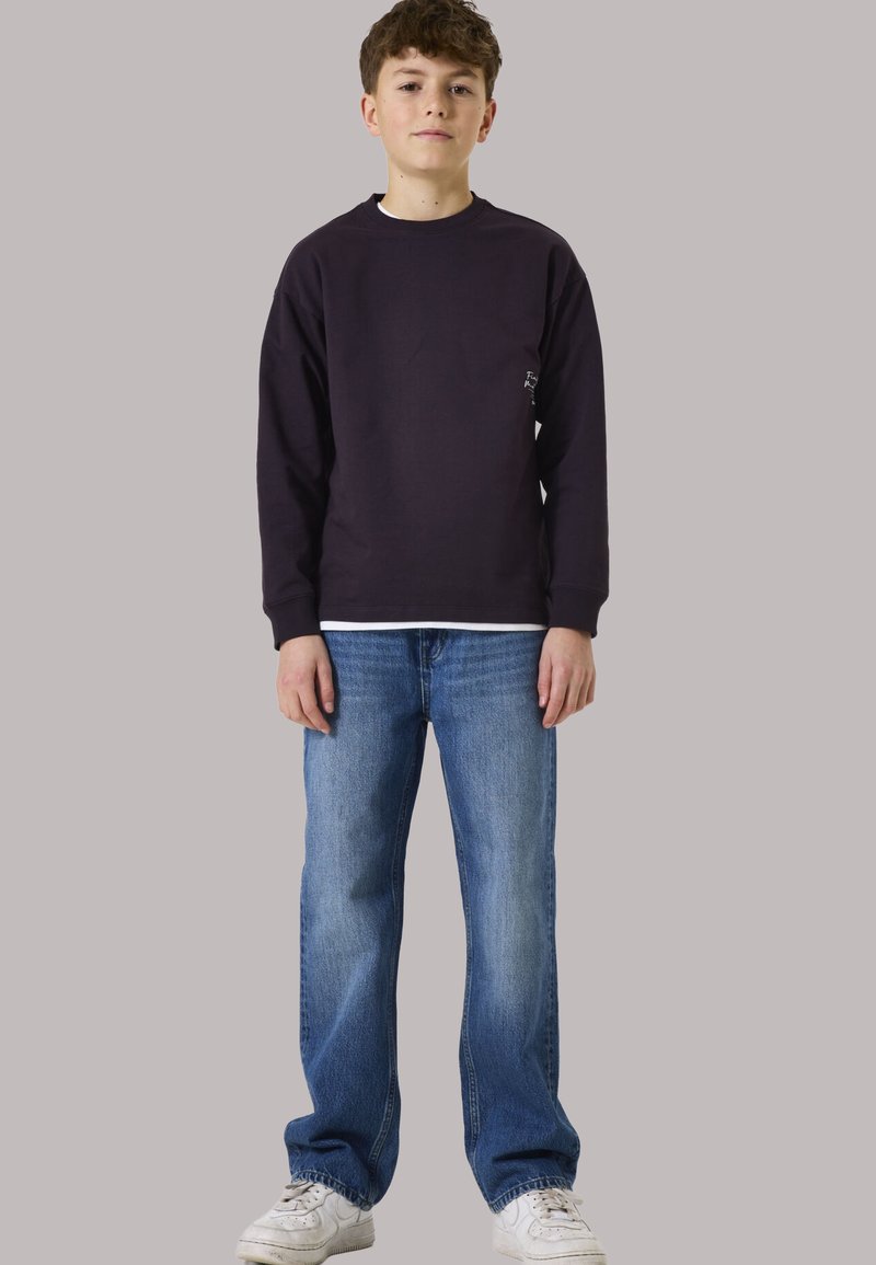 Donkerpaarse sweatshirt met een ronde hals, gedragen over een wit T-shirt, gecombineerd met lichtblauwe traditionele rechte jeans en witte sneakers.
