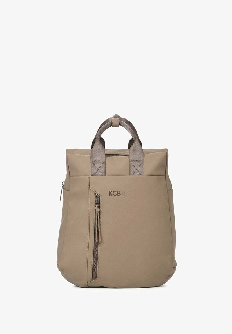 Mochila de tela beige con asa superior, bolsillo lateral con cremallera y logo "KCB" en relieve. Presenta una forma estructurada y una textura suave.
