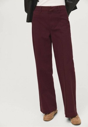 Kvinde iført højtaljede, vidde, burgunderfarvede bukser kombineret med brune loafers og en sort jakke over en hvid top.