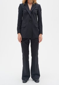 Černý oblek na míru se sakem na jedno knoflík a dvěma předními kapsami, zvanými flared kalhoty, vyrobený z hladké, strukturované tkaniny.