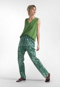 Zielony top bez rękawów z dekoltem w serek, w zestawieniu z luźnymi zielonymi spodniami w botaniczny wzór, dopełniony brązowymi sznurowanymi butami.