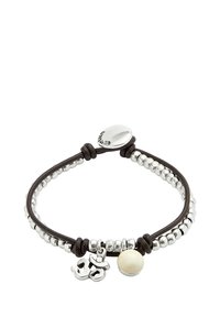 Pulsera de cuentas plateadas con cordón de cuero marrón oscuro, con un colgante metálico y una cuenta de color crema. Cierre ajustable con detalle de logotipo.