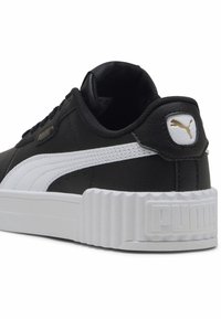 Czarne syntetyczne sneakersy z białymi akcentami, wyposażone w masywną białą podeszwę, teksturowane tylne partie oraz złoty detal z logo po boku.