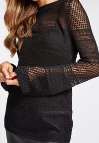 Maglione lungo nero a maniche lunghe con un motivo a tessitura aperta, design testurizzato e una vestibilità rilassata con maniche leggermente svasate.