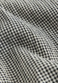 Tissu à petits carreaux noir et blanc avec coutures visibles et plis doux.