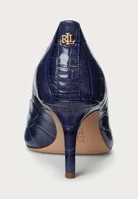 Sötétkék magassarkú cipő krokodil mintával, hegyes orral és fényes felülettel. Arany logó található a hátulján, valamint vékony tűsarkú.