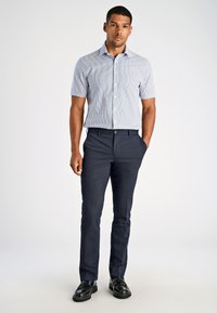 Camicia azzurra a maniche corte con righe verticali, abbinata a pantaloni blu scuro e scarpe nere. Colletto pratico e design aderente.