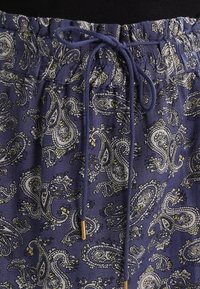 Lila tygkjol med ett paisleymönster i vitt och gult. Elastisk midja med snöre och guldfärgade spetsar.