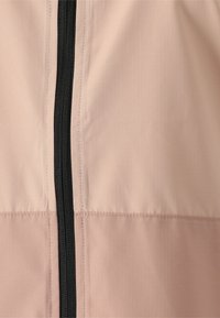 Jasnobeżowa tkanina z dwukolorowym przeszyciem i czarnym suwakiem umieszczonym centralnie, biegnącym pionowo.