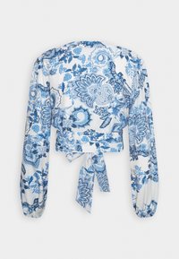 Blusa corta bianca con fantasie floreali blu, maniche lunghe a palloncino e dettaglio con legatura sulla schiena. Presenta una texture di tessuto liscia e leggera.