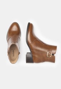Braune Lederknöchelstiefel mit runder Zehenform, niedrigem Blockabsatz und seitlicher Schnallenakzentuierung. Glatte Textur, schlichtes Design, keine sichtbaren Muster.
