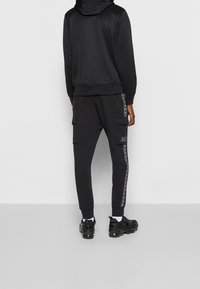 Svart sweatshirt med huva och matchande sweatsbyxor med cargo-fickor, logotypdetaljer och sidostripes i en trendig design.