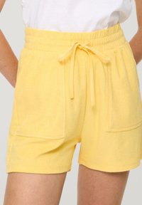 Gele badstof shorts met een elastische tailleband, strikkoord en twee voorkruiszakken. Zachte textuur en losse pasvorm.