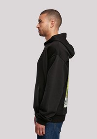 Sudadera negra con bolsillo frontal, mangas largas y capucha. Presenta un diseño gráfico colorido en el costado con una tela texturizada.