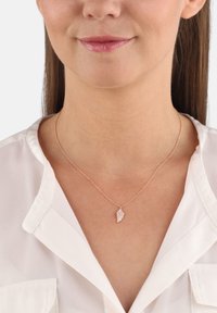 Guldfärgad halskedja med en delikat kedja och ett hänge format som en fjäder. Hänget har små klara ädelstenar för ytterligare detalj.