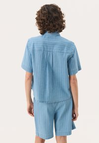Helles blaues Kurzarmhemd und Shorts-Set mit weißen vertikalen Streifen, aus einem weichen, strukturierten Stoff gefertigt. Lässige Passform mit leicht abgerundetem Saum.